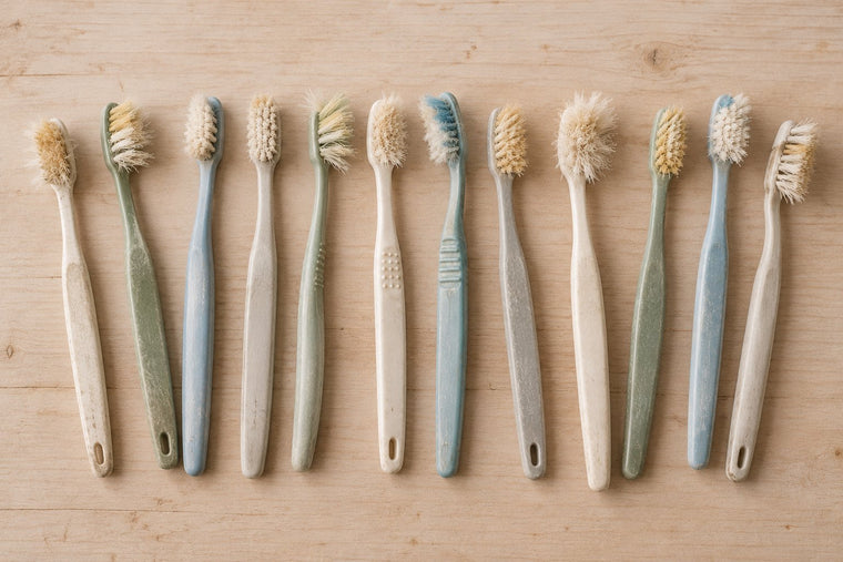 A dozen old, worn plastic toothbrushes in faded colors laid out in a row on a wooden table